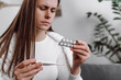 © Yura Yarema - Sick influenza young woman have fever, cough and sore throat, holding thermometer for check measure body temperature, girl hold pill medicine pack reading label text about medical information