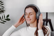 © Yura Yarema - Happy relaxed young woman music fan wearing wireless headphones, sit on sofa, listening to tunes from online player for clear mind, good brain work, mental disease prevention, enjoying leisure