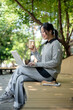 © bongkarn - A woman enjoys a hot drink while working remotely outdoors, sits on a park bench with her laptop.