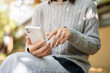 © bongkarn - A woman in cozy clothes sitting on a park bench, enjoys listening to music through her earphones.