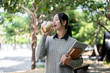 © bongkarn - A charming Asian female college student walks along the footpath on campus, enjoying a hot drink.