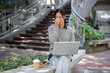 © bongkarn - A tired Asian woman sits outdoors, feeling exhausted and overworked during working on her laptop.