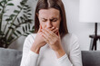 © Yura Yarema - Close up of young woman suffering from nausea at home, caucasian female having morning sickness, ill lady sitting alone on couch in living room, covering mouth