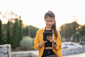 Wall Mural - Smiling young Asian woman using digital tablet in urban city