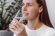 © Yura Yarema - Close up of happy beautiful young woman drinks water from glass sitting on comfortable couch at home, quenches thirst, maintains water balance