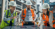 © Gorodenkoff - Crew of Construction and Site Managers Having a Meeting at a Site with Skeleton Frame Building with Concrete and Steel Beams in the Background. Industrial Specialists Using an Interactive Display
