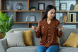© Liubomir - Concerned Asian woman using smartphone with credit card in hand sitting on couch. Concept of online shopping, banking issues, security concern, or financial stress. Focus on phone use.