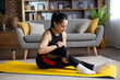 © Liubomir - Asian woman injured while doing fitness and yoga at home, woman strained leg muscle, massaging, muscle pain, sitting on sports mat in living room in apartment.