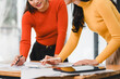 © kenchiro168 - Collaborative work between two women in colorful sweaters, discussing project plans and analyzing documents on table. atmosphere is focused and productive