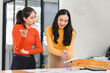 © kenchiro168 - Collaborative business meeting with two women discussing ideas and taking notes. One woman is presenting information while other listens attentively, showcasing teamwork and communication