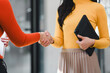 © kenchiro168 - Two women shaking hands in professional setting, one wearing red sweater and other in yellow top, holding tablet. This moment captures collaboration and agreement