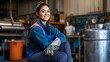 © suyu - Asian Chinese female blue-collar welder in protective workwear smiling and looking away while sitting on a stool in a workshop garage. Skilled tradeswoman in industrial setting, focused on her craft