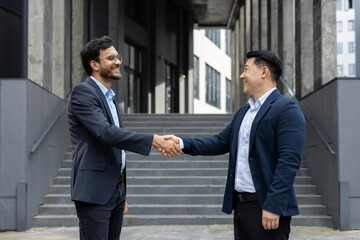 Wall Mural - Businessmen shaking hands outside modern building, symbolizing partnership and success. Their smiles reflect mutual trust, cooperation, and positive business relationships, embodying agreement.