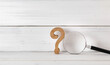 © pachaileknettip - Wooden Question Mark with Magnifying Glass on White Wooden Background Symbolizing Research and Inquiry