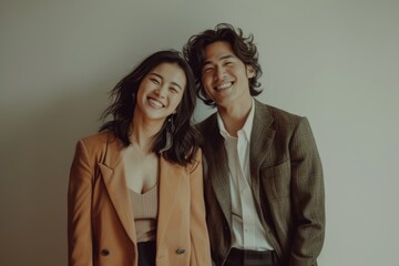 Canvas Print - Portrait of a cheerful asian couple in their 20s dressed in a stylish blazer while standing against bare monochromatic room