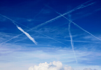 white contrails contrasting with the blue sky and white clouds below