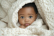 © kazakova0684 - An Afro-American baby wrapped in a cozy white blanket, gazing curiously at the camera