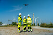 © narong - Wide shot of wind turbine or windmill worker woman or engineer use controller to control the drone to work with her co-worker team in workplace field.
