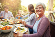 © ReeseFullyOwned/peopleimages.com - Backyard, lunch and portrait of grandma with family for brunch, food and meal together. Christmas, Thanksgiving and grandparents, parents and kids for tradition, festive dinner or celebration in home