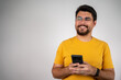 © Nenad - A happy young man in a yellow t-shirt smiling while using his smartphone, texting and enjoying communication in a casual, photogenic studio setting.