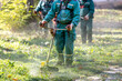 © zphoto83 - Ground workers maintain landscaping by trimming grass with equipment in a green park area during daylight hours