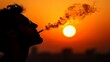 ©  Serhii Hryb - Silhouette of a Person Smoking Against a Vibrant Sunset Sky Showcasing Warm Orange and Yellow Hues