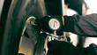 © Iryna - Checking Tire Pressure with a Manual Gauge. A close-up of a gloved hand using a manual tire pressure gauge to measure the air pressure of a vehicle tire.