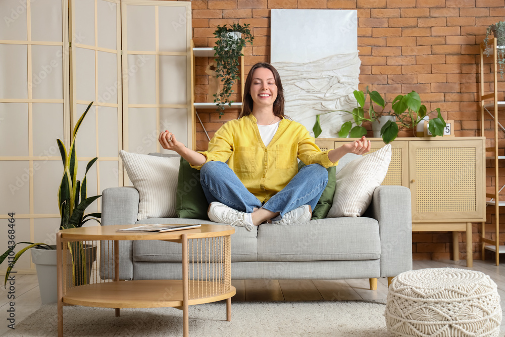 Young woman meditating on grey couch at home