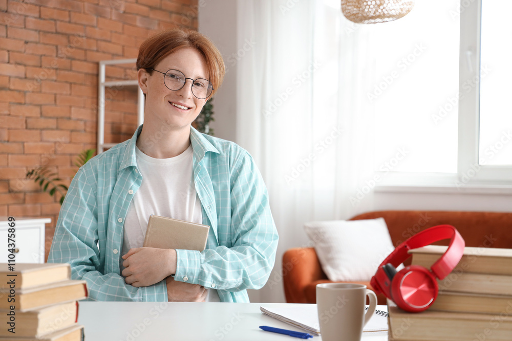 Male student in eyeglasses with book sitting at home