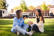 © zvkate - Two women friends sisters sitting in the park and have emotional talk conversation sitting in the grass. Best friends have emotional chat with gesticulating.