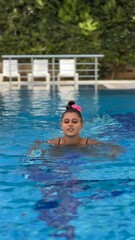 Wall Mural - A girl is swimming joyfully in a pool while wearing a cute pink bow, showcasing summer vibes