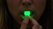 © Viktor_D - Close-up of a young woman holding a glowing green pill between her lips