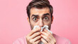 © Sergey - Frustrated sick unhealthy ill allergic man has red eyes runny stuffy sore nose suffer from allergy symptoms hay fever hold paper napkin use nasal drops isolated on pastel pink color background studi