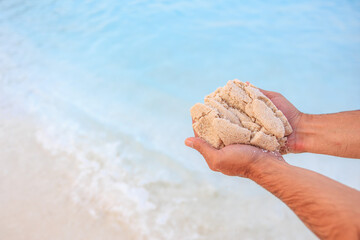 Wall Mural - A man is holding a handful of sand on a beach