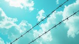 60.A dramatic view of a barbed wire fence cutting across the sky, the metallic strands and sharp barbs clearly visible against a backdrop of fluffy white clouds and a bright blue sky, capturing a