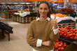 © Grustock - In a vibrant grocery store, a woman stands poised in the background among shelves brimming with fresh vegetables and fruits. The atmosphere feels lively and inviting.