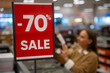 © Grustock - Shoppers explore a retail store with significant discounts. A woman examines shoes while a vibrant sale sign highlights a 70 percent reduction on prices, attracting eager buyers.