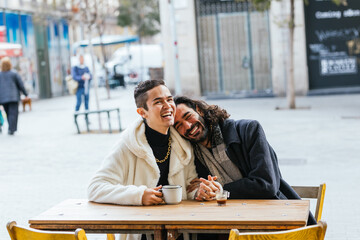 Wall Mural - Gay couple laughing and having coffee at outdoor cafe