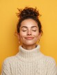 © Johannes - Happy calm patient young woman makes zen nirvana gesture meditates with closed eyes practices yoga has combed hair wears earrings and casual jumper smiles happily isolated over yellow background.