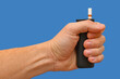 © Kryuchka Yaroslav - A device for electrically heating tobacco with a stick is held in the hand against a blue background.