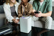 © pressmaster - Group of three people engaging with smart speaker placed on a table using smartphone, showing interaction and conversation with the device