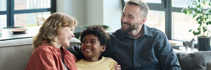 Wall Mural - Family members cuddling on a cozy couch in bright room. They are smiling, spending time together, and enjoying natural light coming through the windows