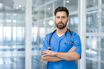 Wall Mural - Confident male nurse wearing with stethoscope in modern hospital. He stands with arms crossed, portrays professionalism and trust in healthcare environment.