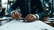© altitudevisual - Close-up of a business person in a suit signing a document with a pen at a desk