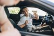© Maskot - Happy young man showing drivers license while sitting in car