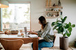 © Maskot - Side view of focused businesswoman working on laptop while sitting near dining table in living room at home