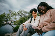 © Maskot - Low angle view of smiling teenage girl using smart phone while sitting with male friend
