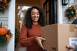 © Milos - A joyful woman receiving a package at her front door, embodying the excitement of online shopping and the convenience of home delivery during the autumn season.