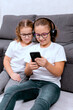 © Лиза Птицына - Two girls use a parental control app on a phone, playing a kids' game and sharing a gadget while relaxing at home. Perfect for themes about safe content, parental control, and technology.