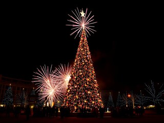 fireworks are lit up in the dark near a christmas tree.